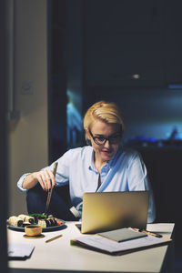 Businesswoman looking having food while using laptop computer at desk in home office