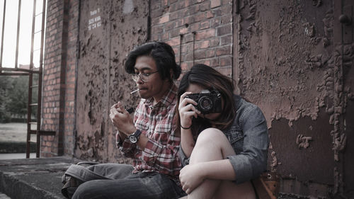 Portrait of young woman photographing against wall