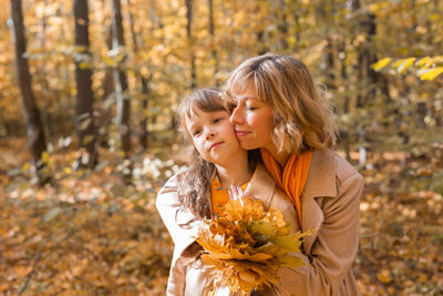 Mother and girl standing by tree during autumn
