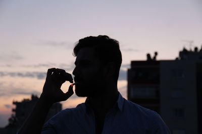 Man smoking cigarette against sky during sunset