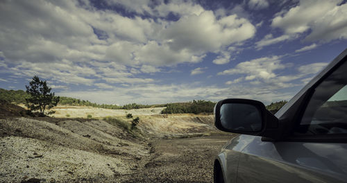 Car rearview mirror on the plain with the pine forest in the background and the sky with clouds