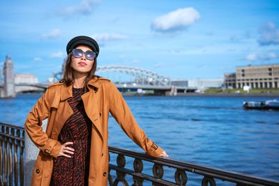 Beautiful woman in a cap and jacket posing while standing on the embankment