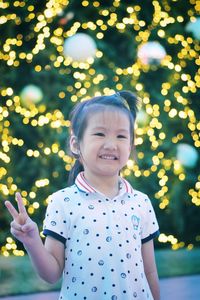 Smiling girl gesturing while standing against illuminated christmas tree