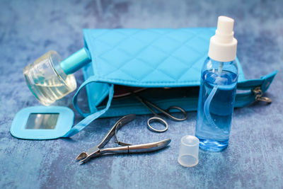 Close-up of small spray bottle with clutch bag and tweezers on blue table