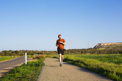 Man standing on footpath against clear blue sky