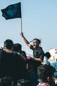 Man holding flag while screaming against sky