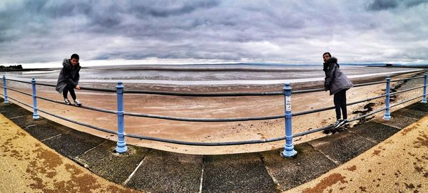 People standing on railing against sea