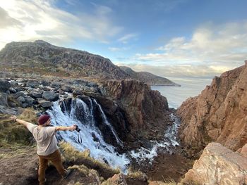 Rear view of man on rock in sea against sky