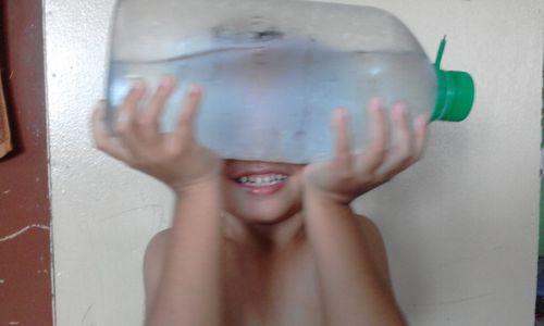 Shirtless boy holding bottle with water against wall
