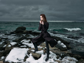 Woman on rock at beach against sky