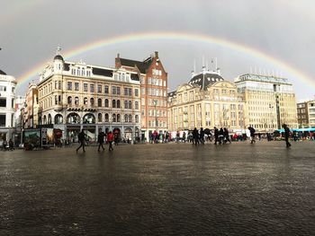 People on wet street in city with rainbow against sky during monsoon