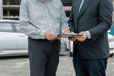 Midsection of man holding mobile phone while standing in car