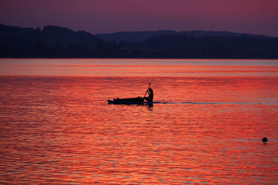 Silhouette people in boat on sea against sky during sunset