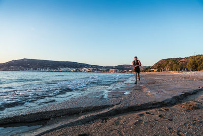 Man is jogging on jogging the beach against clear blue sky in the early morning