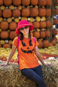 Portrait of smiling woman wearing hat standing against pumpkins