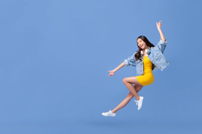 Full length of woman jumping against clear blue sky