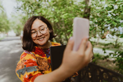 Happy adult woman taking a selfie with her mobile phone in blooming park.