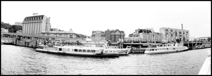 Boats in river by city against clear sky