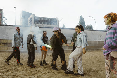 Gay man holding distress flare with non-binary friends standing on sand at park