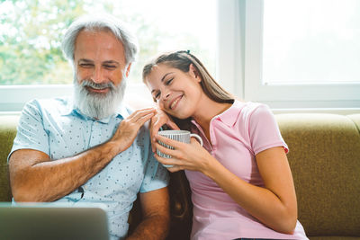 Smiling friends using phone while sitting on sofa at home