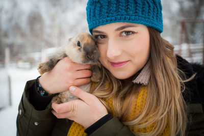 Close-up portrait of woman holding rabbit while standing on field during winter