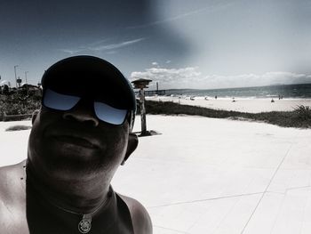 Portrait of young man wearing sunglasses at beach against sky