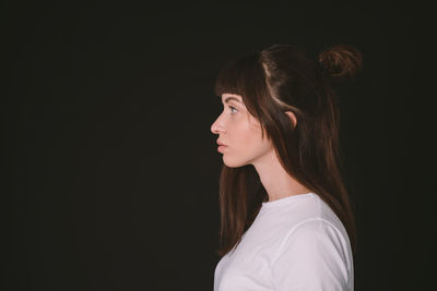 Portrait of teenage girl looking away against black background