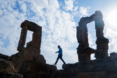 Low angle view of man standing on rock against sky