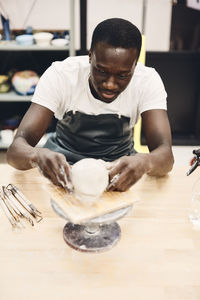 Young man wearing apron molding clay sitting at table in art class