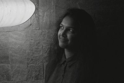 Smiling young woman looking at pendant light against wall in room at home