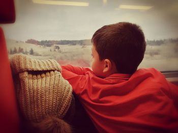 Rear view of boy looking through window while traveling in train