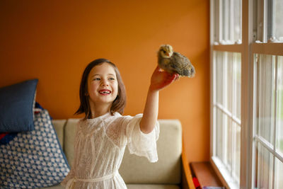 A joyful child holds a small fluffy baby chicken aloft in her hand