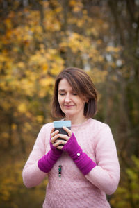 Portrait of woman holding camera while standing during autumn