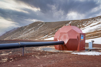 Metallic round duct at krafla geothermal power plant by mountain against sky