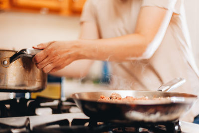 Young millennial woman at home in the kitchen cooking  on gas stove or range 