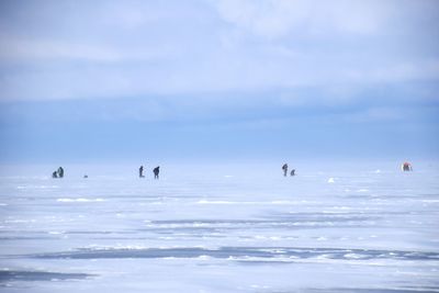 People on frozen lake against sky during foggy weather