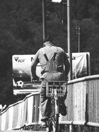 Rear view of man with bicycle standing on railing