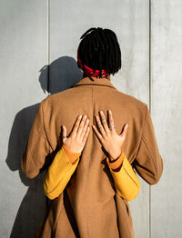 Back view of cool ethnic man with dreadlocks and in coat embracing with faceless female with hands on back