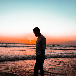 Silhouette man standing on beach against sky during sunset