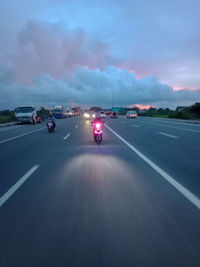 Vehicles on road against cloudy sky