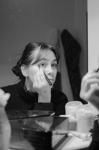 Young woman applying make-up in front of mirror