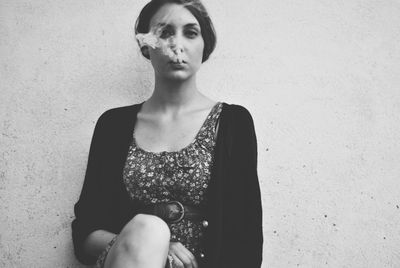 Close-up portrait of young woman exhaling smoke against wall