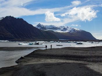 People standing at riverbank against sky