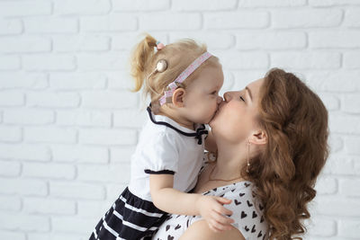 Side view of mother kissing daughter against wall