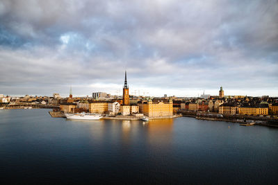 View of buildings by river against cloudy sky