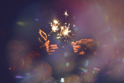 Close-up of people holding lit sparklers at night