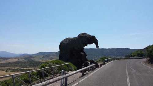 Road leading towards mountains against clear blue sky