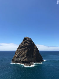 Rock formation in sea against blue sky