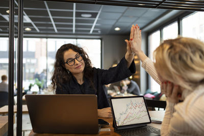 Female coworkers doing high five in cafe