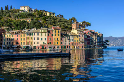 Buildings by canal against clear blue sky